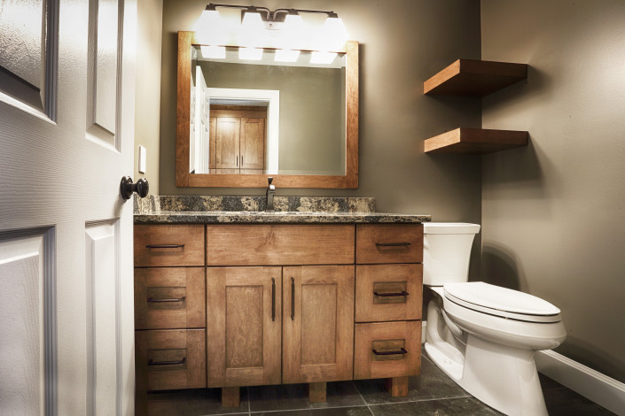 Warm wood vanity. Chunky shelves above toilet. Chunky legs on vanity base. By House of J Interior Design. Edmonton, Alberta.