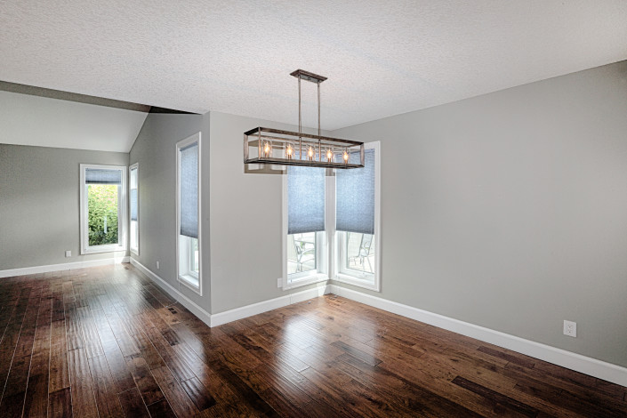 View of the dining room leading to the living room. New hardwood floors, baseboards, window casings, light fixture and paint. By House of J Interior Design. Edmonton, Alberta.